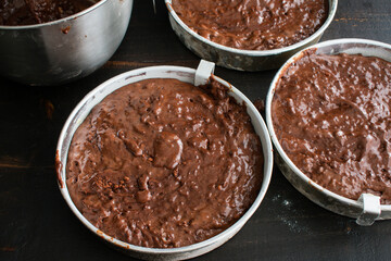Cake Pans Filled with Chocolate Batter: Three greased and floured aluminum cake pans filled with chocolate cake batter