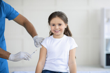 African American doctor making coronavirus vaccine injection to little girl at clinic, panorama
