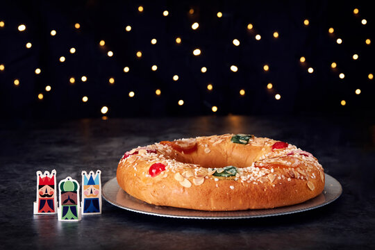 Christmas scene..Three Kings cake with candied fruit and almonds on a gray plate. Three figures of the three wise men to one side. In the background Christmas lights.