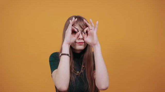 Making glasses of fingers, looking at camera and smiling, funny, hold hands near eyes, imitating binoculars, holding arm eyebrows, through imaginary binocular, grimacing, mask with hand.