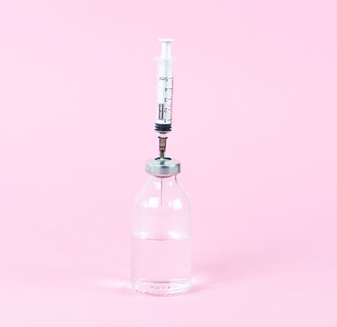 A bottle with a liquid and a syringe on a light pink background.