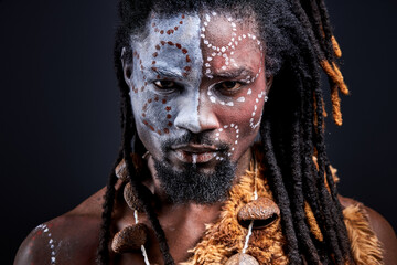black shaman with national ethnic make-up on body, face. young male with dreadlocks is confident in...