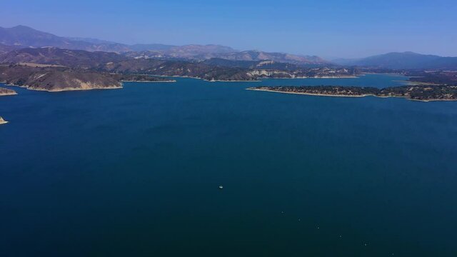 Wide angle aerial shot of Lake Cachuma outside of Santa Barbara Ca. Beautiful blue water and sky with no clouds and mountains in the background.