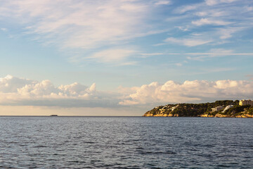 view from the sea to the steep coast with hotels on the Greek island of Crete against the backdrop of a blue cloudy sky
