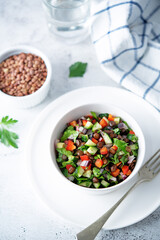 Green lentil red bell pepper cucumber parsley salad in a bowl