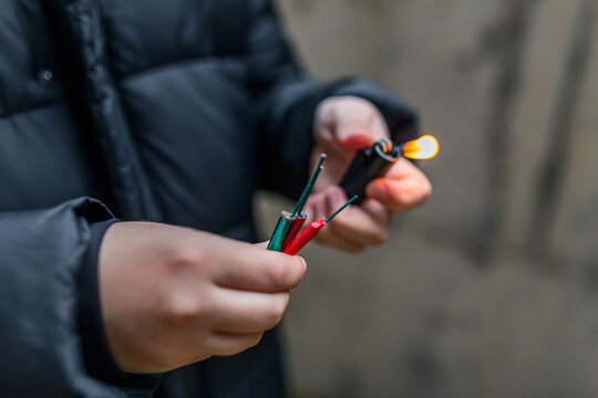 Boy lighting up several firecrackers in his hand using lighter. Kid getting ready for celebration with fireworks or pyrotechnic products . Boy holding a burning petard in his hand. Close up shot