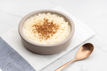 Creamy rice pudding with cinnamon in bowl on white marble table