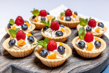 Fruit and berry tartlets dessert assorted on wooden tray. Closeup of delicious pastry sweets pies colorful cakes with fresh natural raspberry blueberry and cheese cream. French bakery catering.