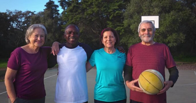 Group of seniors embracing holding basketball on outdoors court