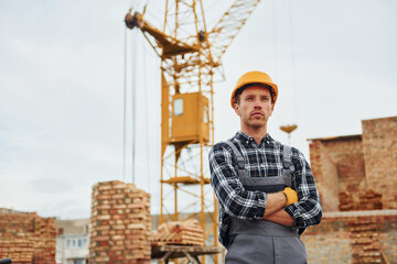 With arms crossed. Construction worker in uniform and safety equipment have job on building