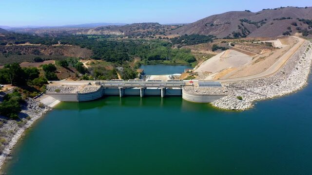 Aerial fly over shot of Lake Cachuma and the Bradbury Dam near Santa Barbara Ca. with clear blue sky, mountains, and no clouds.
