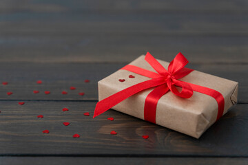 close up image of wrapped giftbox tired up with red ribbon lie on wooden background with little red hearts near.. Copy space for text. Valentines day concept