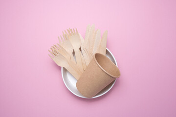 Wooden and cardboard disposable tableware on a pink background. Environmentally friendly products.