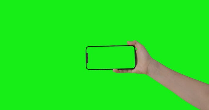 iPhone 12 Pro Max isolated on chroma key. Woman hand hold phone with a green screen in a horizontal orientation landscape mode. Mockup for compositing.