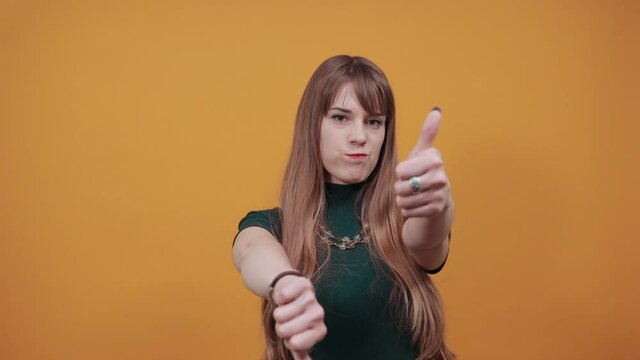 Human hand thumb down, no okay sign, angry face, negative gesture showing dislike with finger, rejection. Young attractive woman, dressed green shirt blonde hair, yellow background