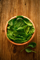 Fresh spinach in a ceramic bowl on a wooden background, top view