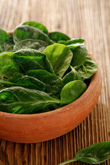 Fresh spinach in a ceramic bowl on a wooden background, close up view