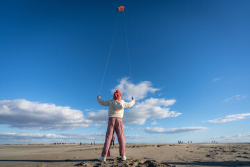un enfant de dos avec un bonnet rouge, joue avec un cerf volant sur une plage