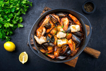 Traditional French seafood bouillabaisse with fish, king prawns and mussels in red wine sauce as top view in a modern design pot