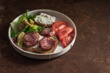 English breakfast with scrambled eggs, sausage, toast and fresh salad on a white plate on an aged rusty background. Copy space