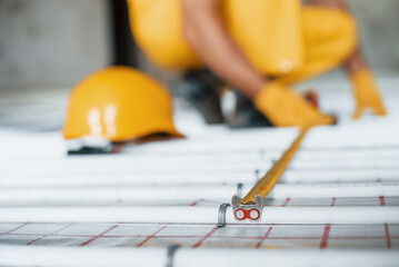 Close up view. Worker in yellow colored uniform installing underfloor heating system
