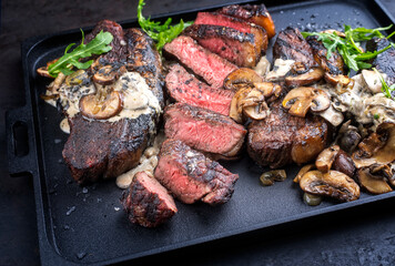 Modern style barbecue dry aged wagyu Brazilian picanha steaks from the sirloin cap of rump beef sliced and served cream sauce and mushrooms as top view on a design tray