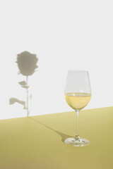 Wine glass with a shadow of a rose on yellow background. Minimal holiday concept. Valentine celebration idea.