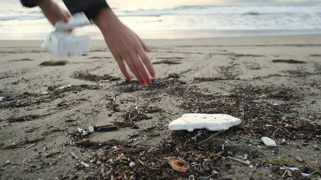 Young woman pick up polystyrene plastic from dirty ocean coast after sea storm,environmental protection concept