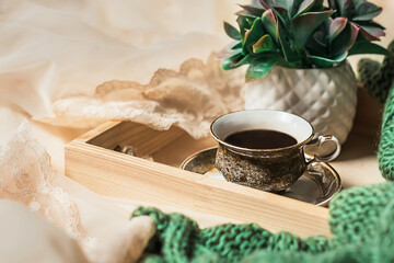 Morning coffee. A cup of coffee on a wooden tray on a silk bed with a knitted blanket. Home cozy interior, lifestyle, romantic atmosphere.