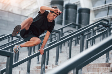 Doing parkour. Young man in sportive clothes have workout outdoors at daytime