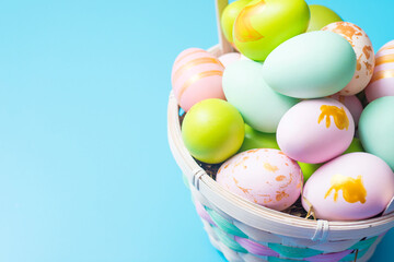 Easter basket filled with painted Easter Eggs over a blue background. Colorful painted easter eggs in basket on blue background