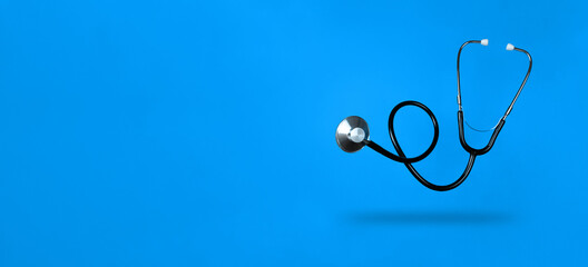 Levitating stethoscope on blue background and shadow under it with copy space. Stock photo.