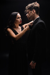 elegant woman with red lips looking at man and pulling hair on black