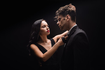brunette woman with red lips looking at man and pulling hair isolated on black