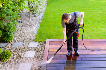 power washing - man worker cleaning terrace with a power washer - high water pressure cleaner on wooden terrace surface - 403112590