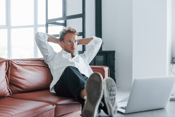 With laptop. Caucasian young guy in elegant white shirt indoors at home