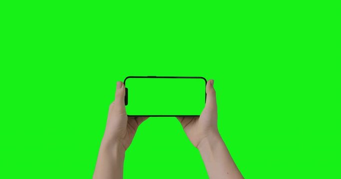 iPhone 12 Pro Max isolated on chroma key. Woman hands hold a phone with a green screen in a horizontal orientation landscape mode. Mockup for compositing.
