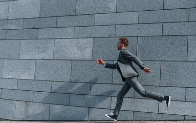 Running and late for the work. Young successful businessman in grey formal wear is outdoors in the city