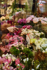 Florist takes flowers out of the fridge. Flower seller chooses flowers for future bouquet. Flowers shop worker in a mask standing in flower refrigerator and checking flowers in glass vase.