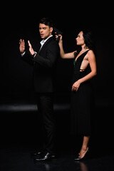 full length of dangerous woman holding gun while aiming in man on black