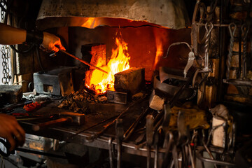 blacksmith holds billet over hot coals in clay oven. blacksmith heating iron metal sword manufacturing marching forge, Hands of blacksmith holding steel in fire of a red-hot forge