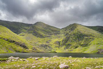 Green island on Lough Callee and waterfalls on mountainside at foothill of tallest Irish mountain, Carrauntoohil in Ring of Kerry, Killarney, Ireland