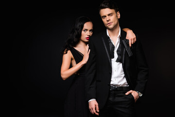 dangerous woman holding gun and hugging man in suit isolated on black