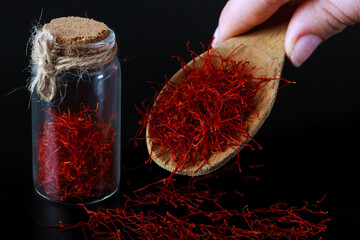 dry spice saffron in a glass bottle and on a wooden spoon on a black background
