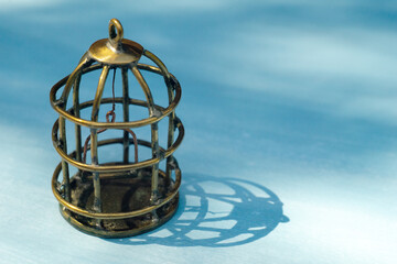 Empty miniature bird cage, made of brass wire, on blue isolate