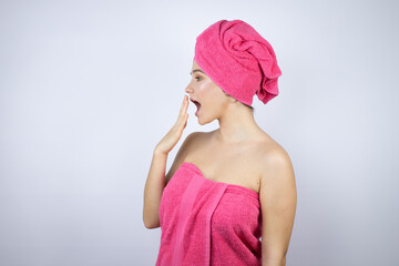 Young beautiful woman wearing shower towel after bath standing over isolated white background with her hand over her mouth and surprised, looking side