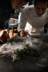 men chefs sprinkle on magnificent molecular cuisine dish decorated with pine branches