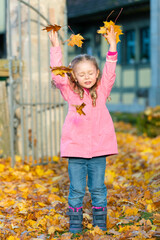 girl in a pink jacket playing with leaves in an autumn park