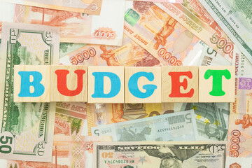 The inscription budget in multicolored cubes on the background of banknotes euro dollars rubles