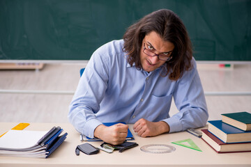 Young male teacher in front of green board